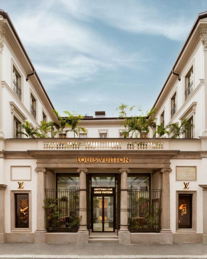 Fachada do edifício de estilo clássico da Louis Vuitton, com logotipo em destaque e plantas ao redor na entrada.