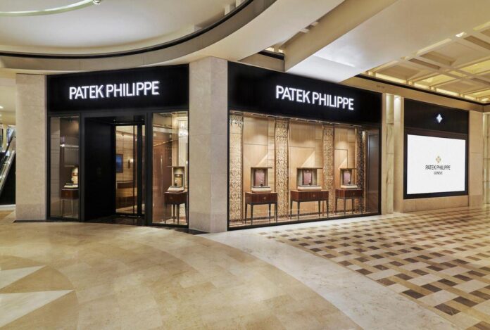 Imagem interior da boutique da Patek Philippe com paredes de mármore claro e vitrines de relógios.