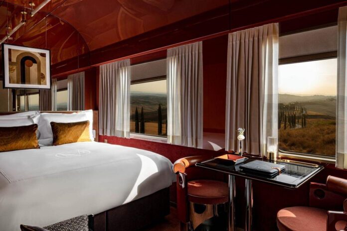 Quarto luxuoso com vista para uma paisagem natural de campos e ciprestes.
