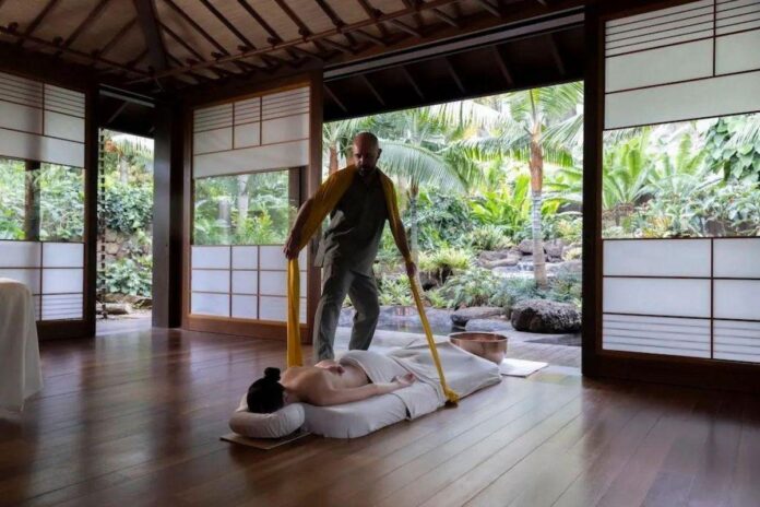 Terapeuta realizando massagem em ambiente natural, cercado por plantas tropicais e com luz natural.
