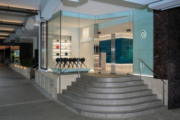 Um ambiente urbano, com piso de pedra e áreas bem iluminadas ao redor. - fachada em vidro, escadas em mármore, exibições de produtos coloridos, logotipo da Devialet