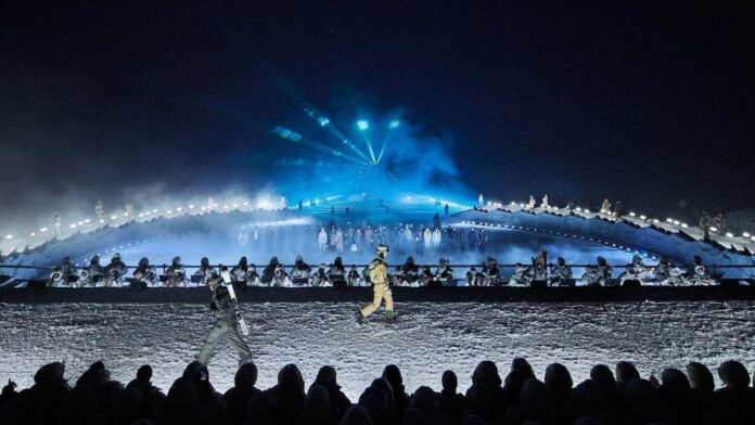 Um cenário montanhoso noturno, com uma pista elevada e uma audiência visível na frente. - luzes azuis, modelos vestindo roupas de inverno, névoa, cenário ligado à montanha