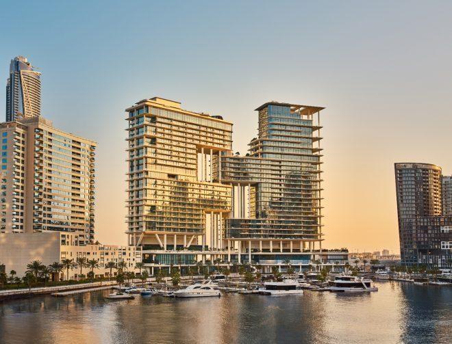 Vista lateral do exterior do The Lana com iates e um horizonte de Dubai ao fundo. Esta imagem reflete o luxo e a sofisticação do local, destacando o ambiente urbano ao pôr do sol.