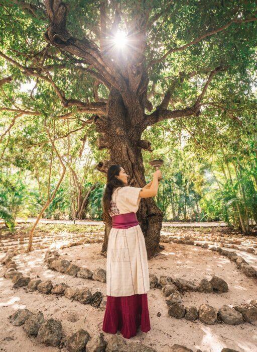Cerimônia do cacau, com uma mulher vestindo roupas tradicionais mexicanas em um cenário natural.