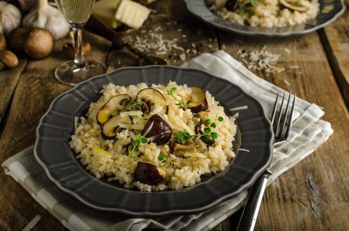 Risoto italiano original com cogumelos e queijo parmesão, servido em uma mesa rústica com ingredientes ao redor.