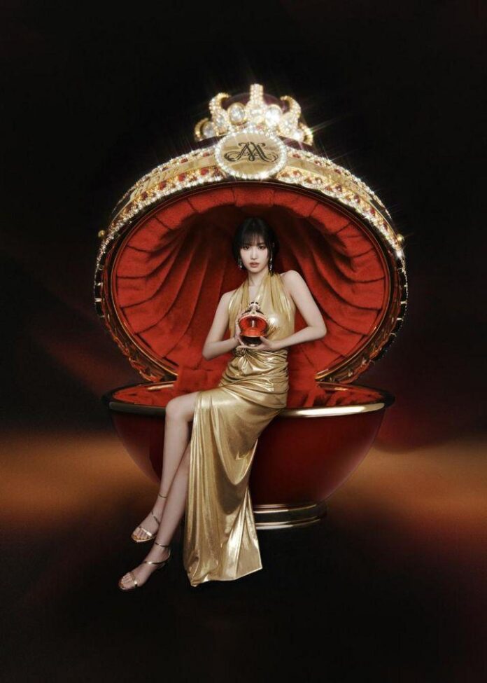 Uma mulher em um vestido dourado segurando um frasco de perfume luxuoso em um fundo escuro, destacando detalhes dourados e brilhantes.